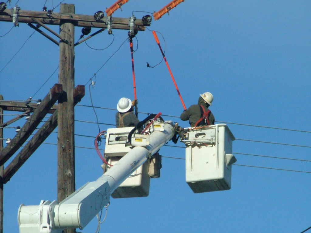 Two linemen in cherry pickers working on a line with a blue sky in the background