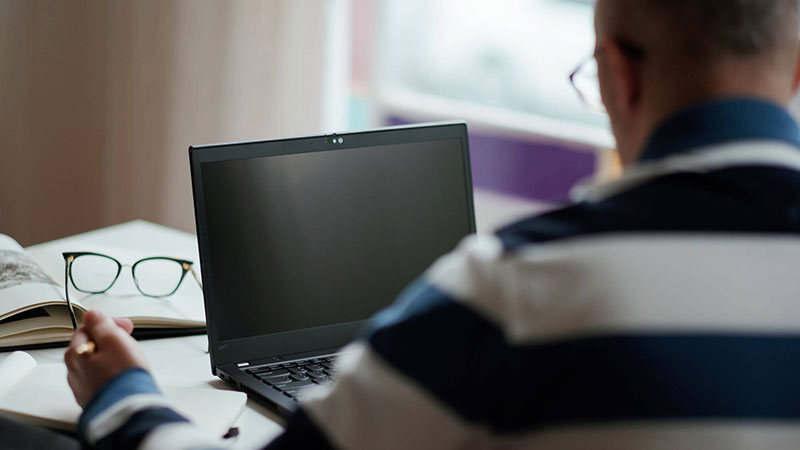 A consumer sitting behind a computer with a pair of reading glasses in the background